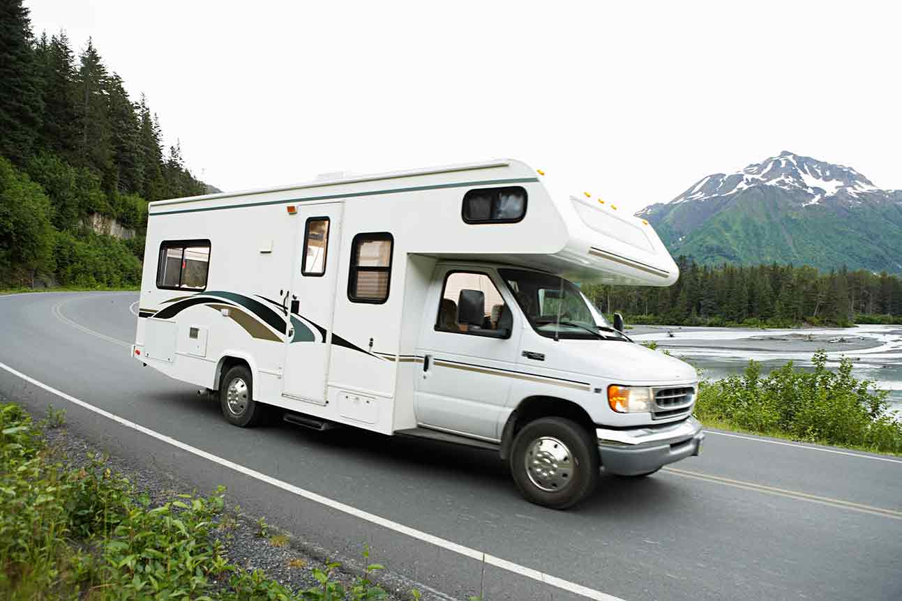 Recreational vehicle driving on road — in West Springfield, MA White RV driving on a road along a river, mountains in background.