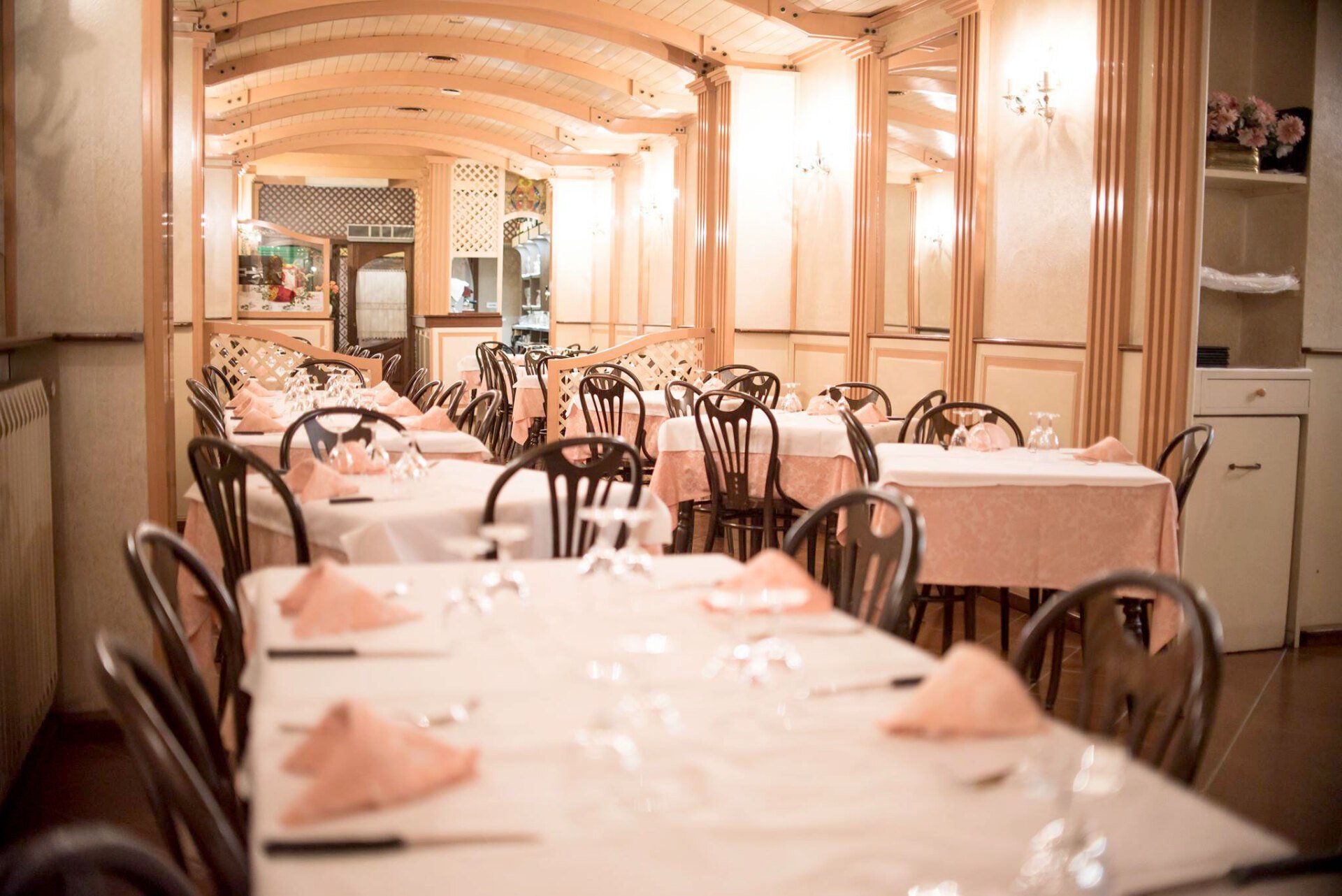 Interno del ristorante con tavoli apparecchiati per la cena; tovaglie rosa chiaro, sedie in legno, luci soffuse.