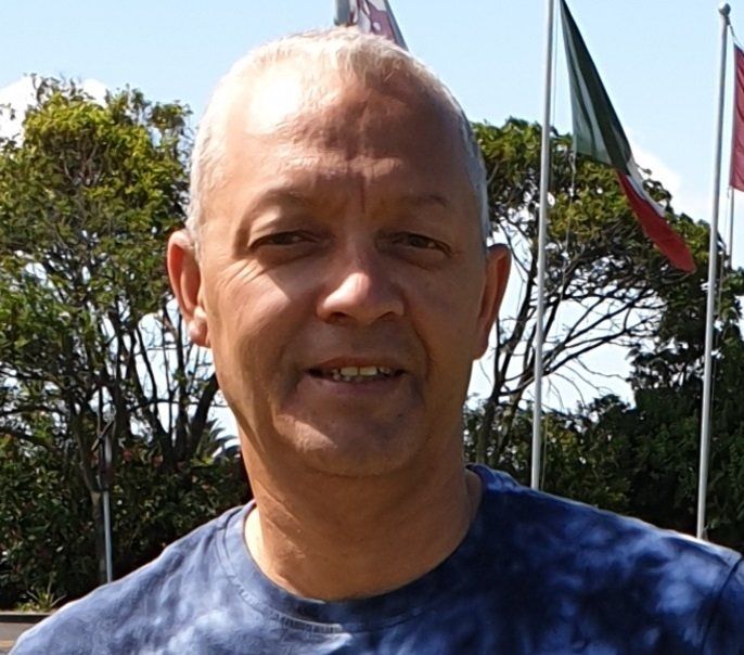 A man in a blue shirt stands in front of flags