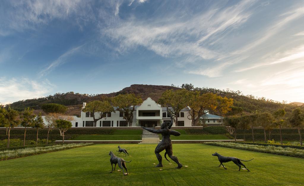 A statue of a man playing with two dogs in front of a large house.