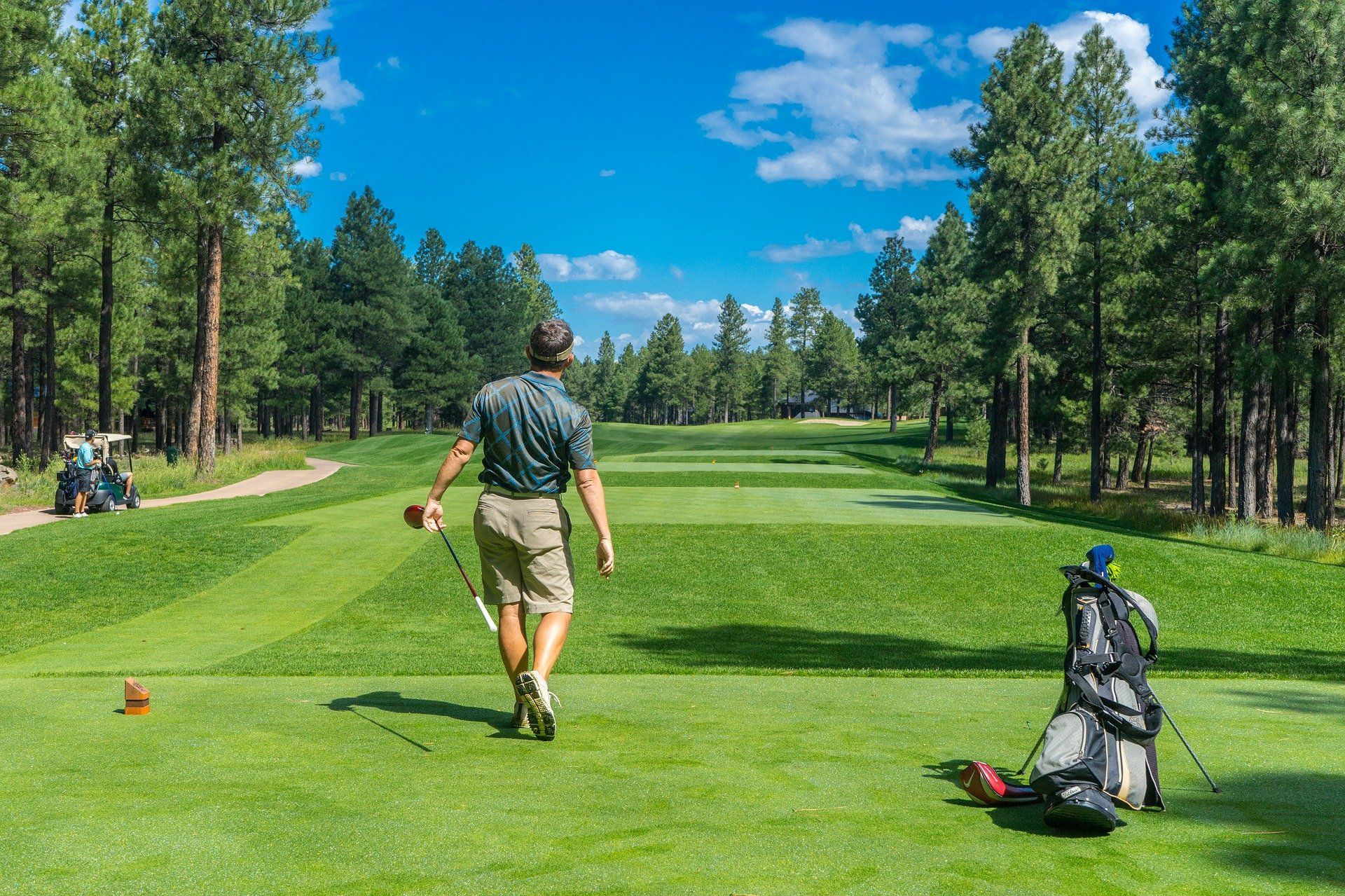 A man is walking down a golf course with a golf bag.