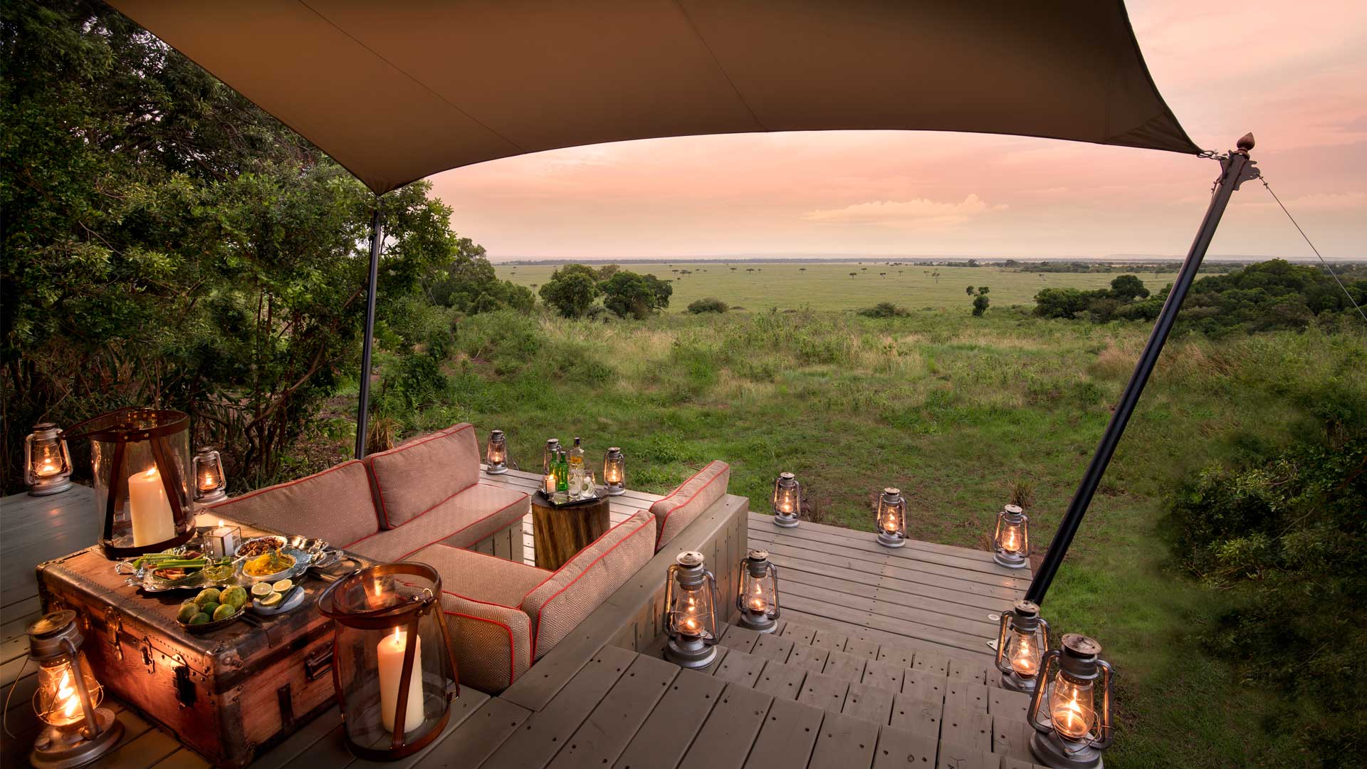 A deck with a couch and lanterns on it overlooking a grassy field