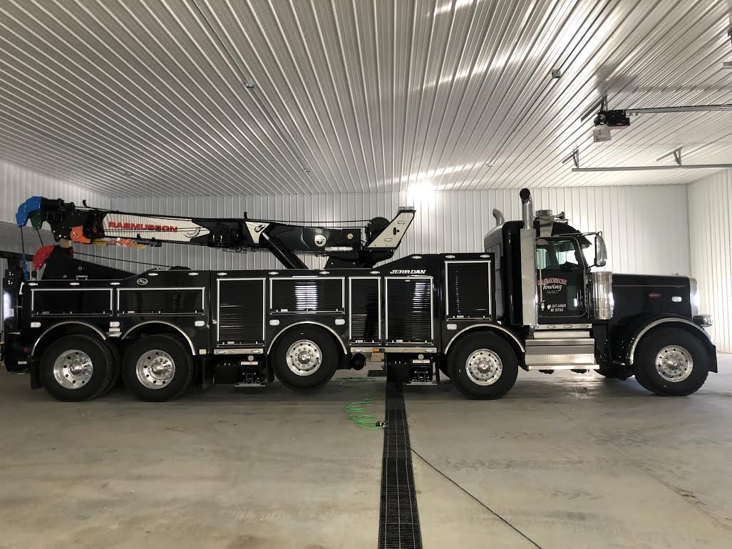 A large black tow truck is parked in a garage.