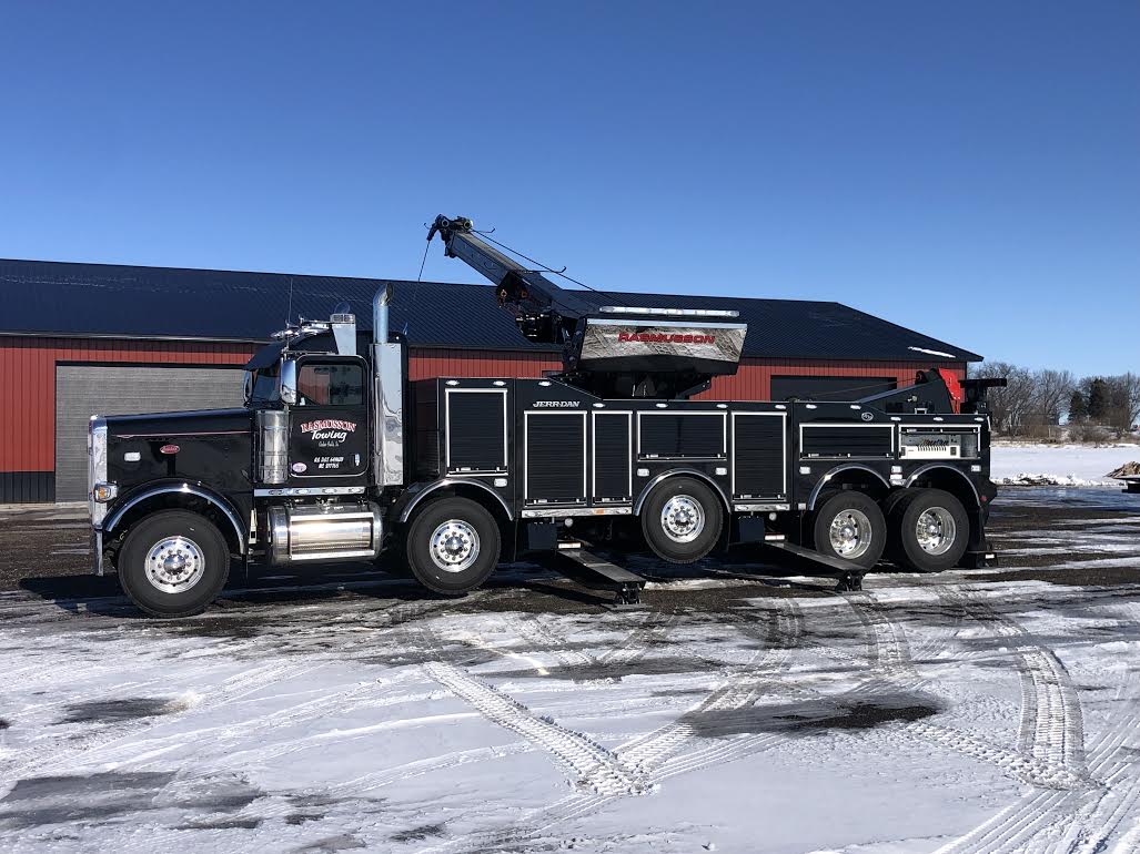 A black tow truck is parked in the snow in front of a building.