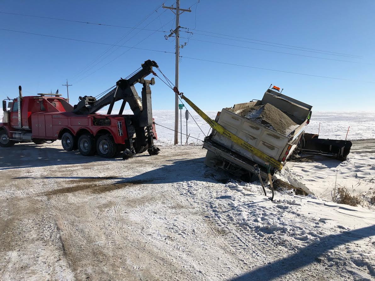 A tow truck is pulling a truck that is stuck in the snow.
