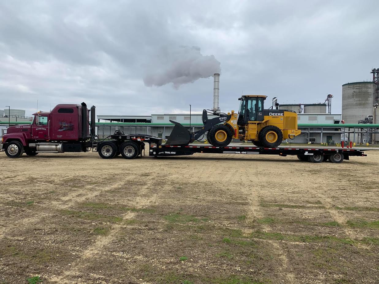 A red semi truck is carrying a yellow bulldozer on a trailer.