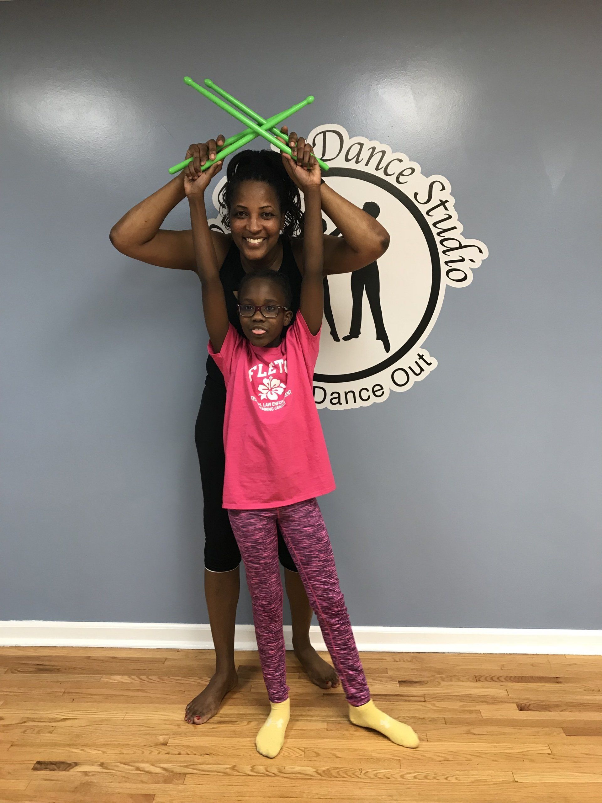 Two children posing in dance costumes with crossed neon-green sticks in a dance studio
