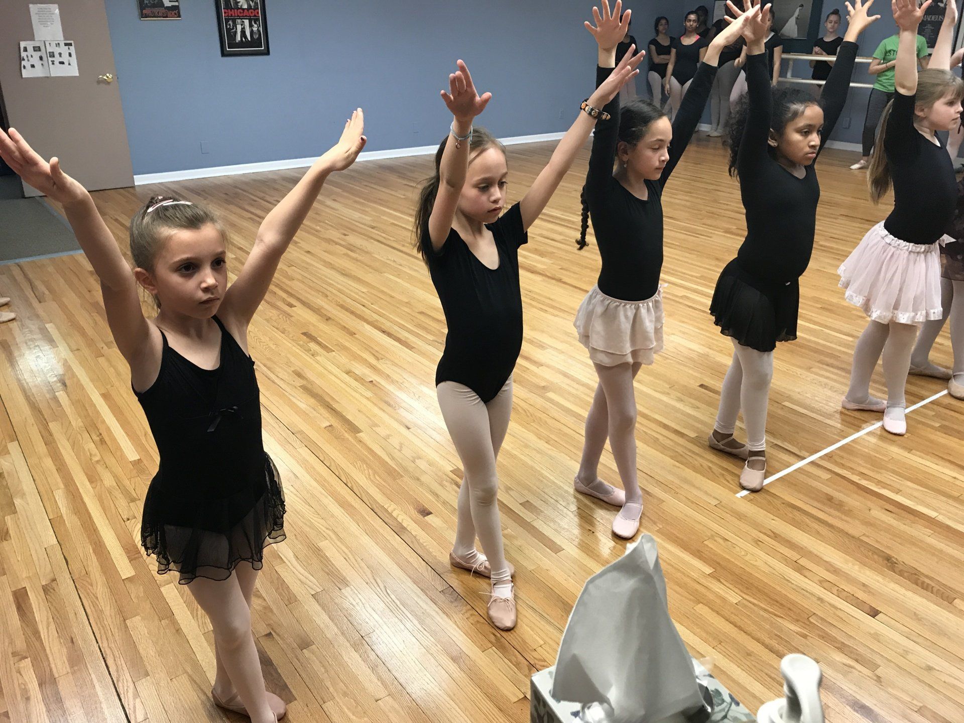 Children in dance class practicing ballet poses in a studio with wooden floor