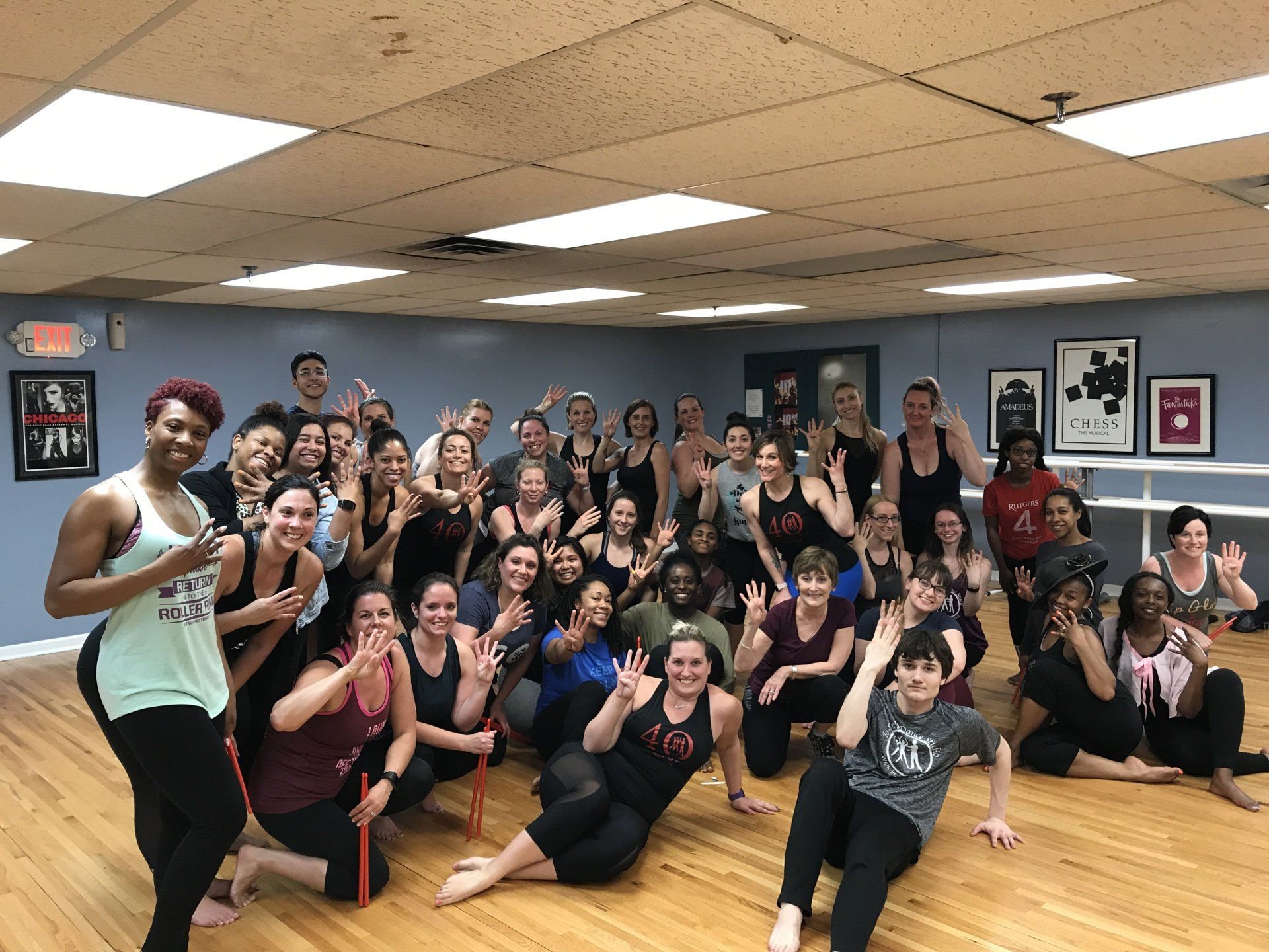 Large dance class group posing together in a mirrored studio, smiling and flashing peace signs.