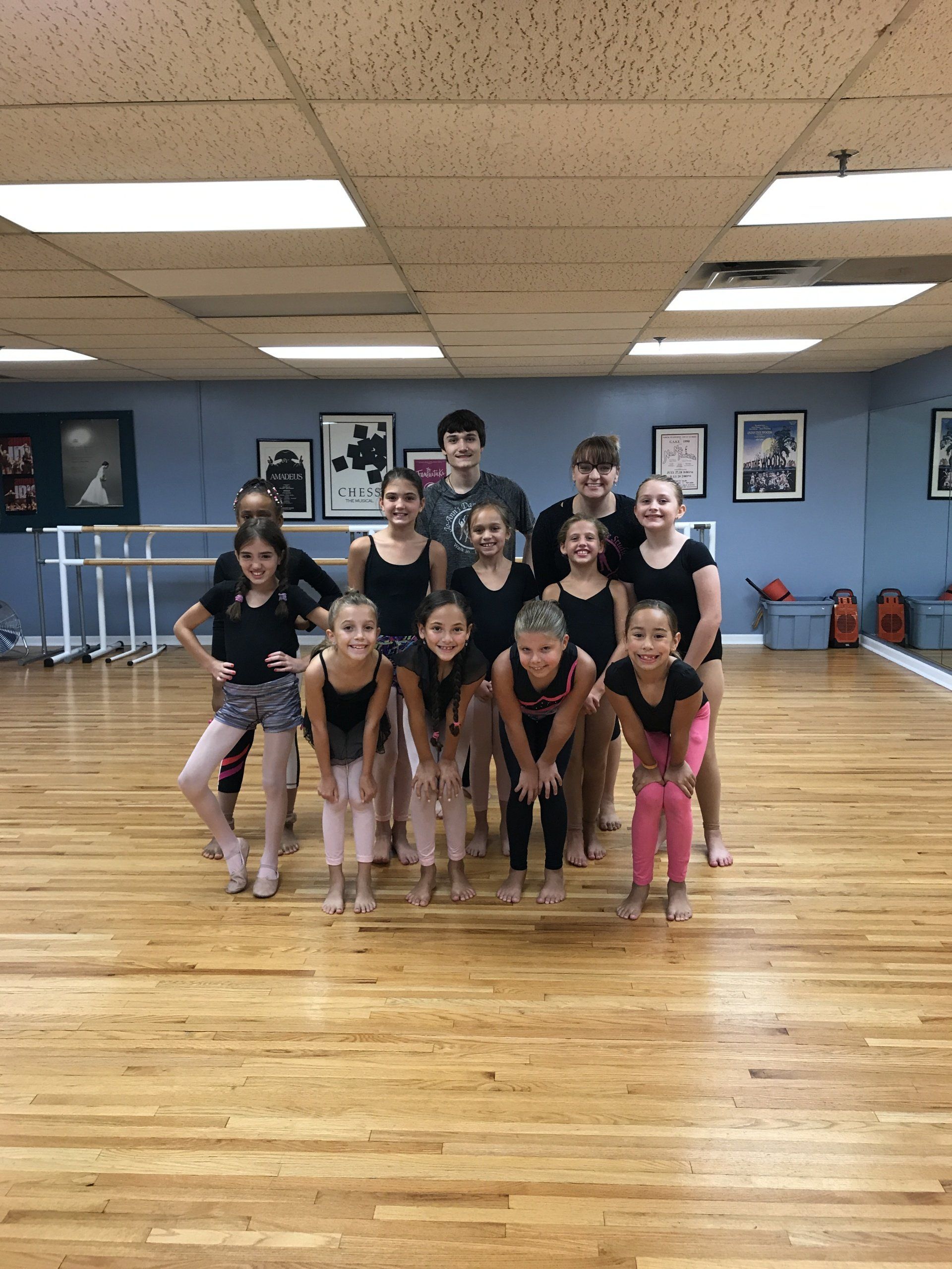 Group of dancers posing in a studio, wearing black and pink outfits on a wooden floor.