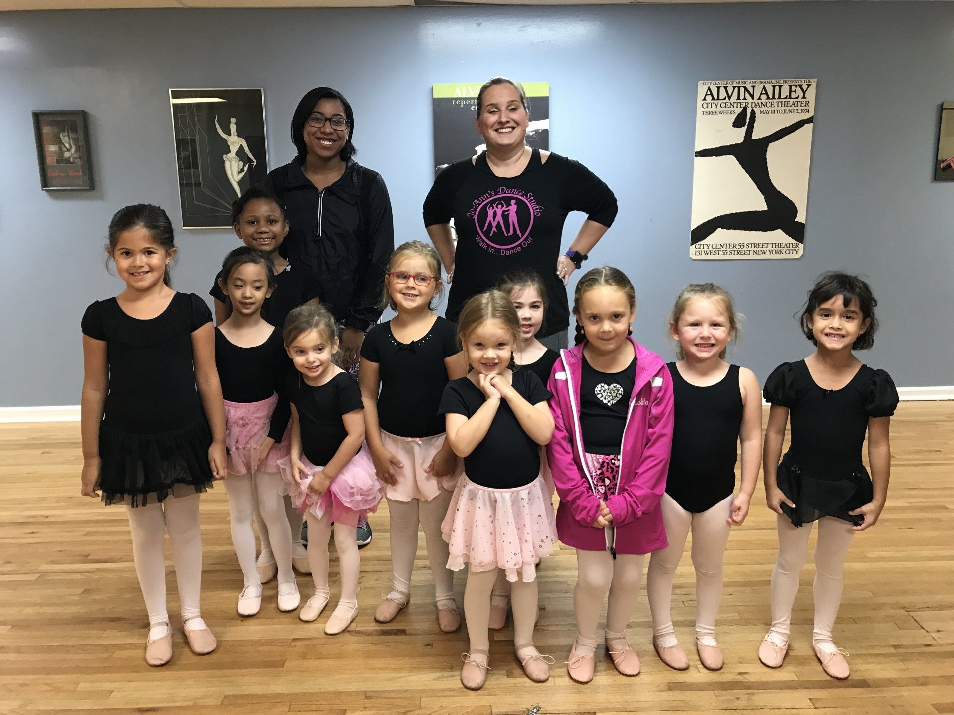 Group of ballet dancers posing in a studio, wearing black and pink leotards and tutus.