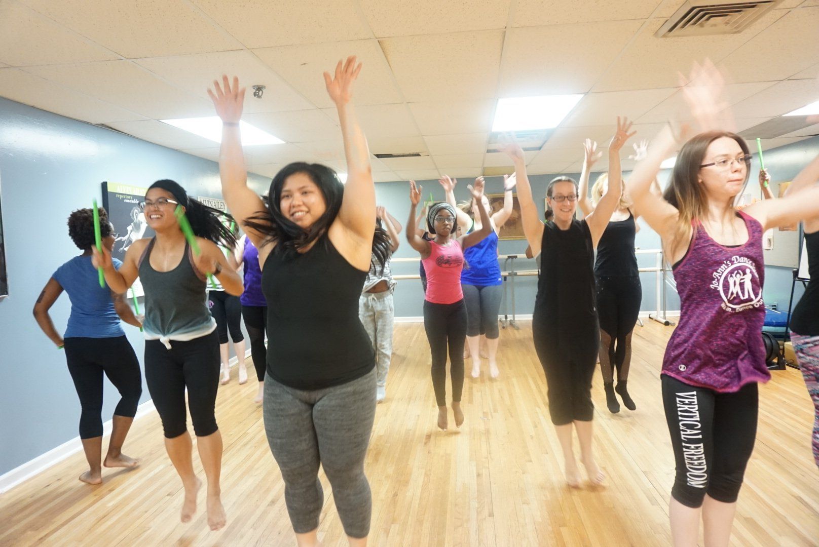 People exercising in a dance fitness class with arms raised in a bright studio