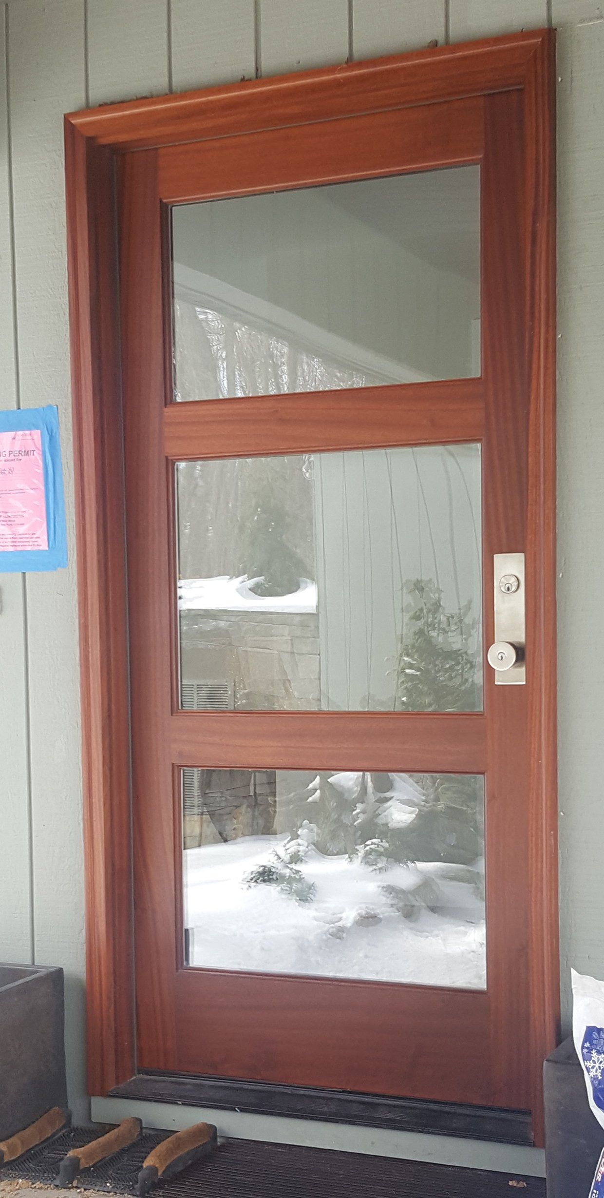 A wooden door with a lot of glass is sitting on a porch.
