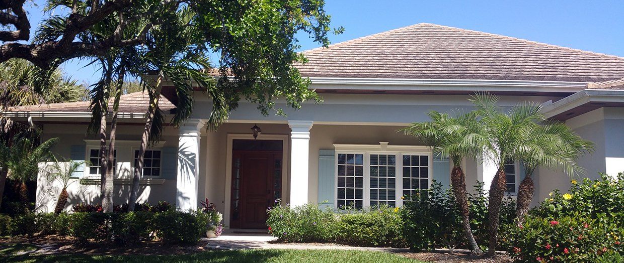 A white house with a tile roof is surrounded by trees and bushes.