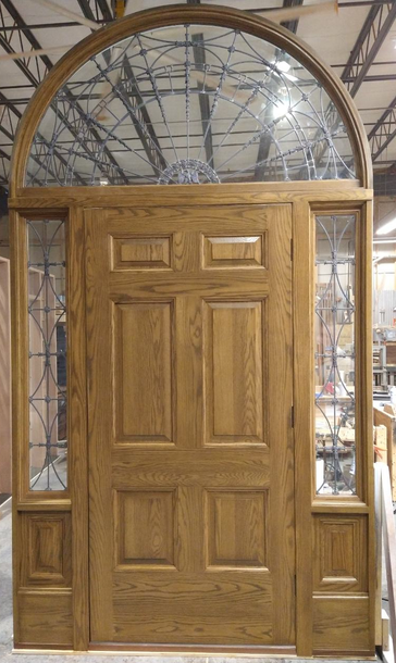 A wooden door with a glass arch over it is sitting in a room.