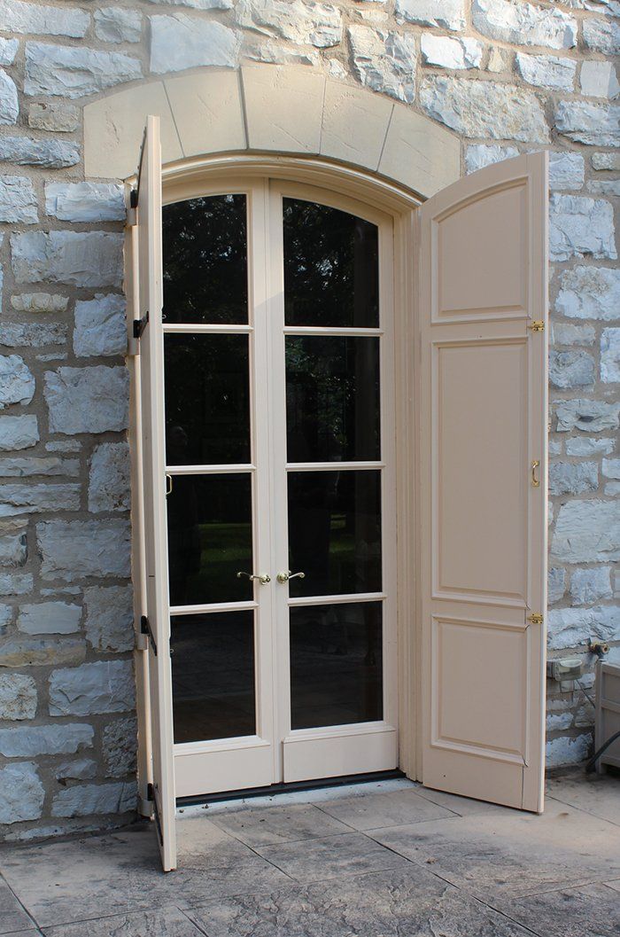 A door with shutters is open on a stone wall.
