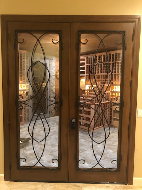 A wine cellar with a wrought iron door and glass doors.