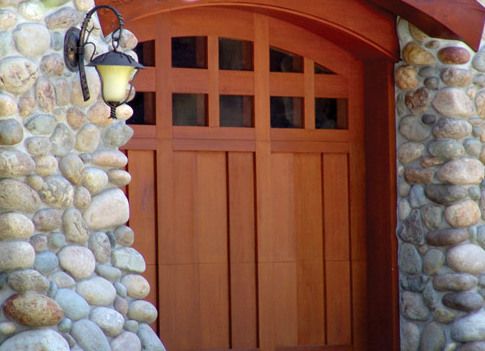 A wooden garage door is next to a stone wall