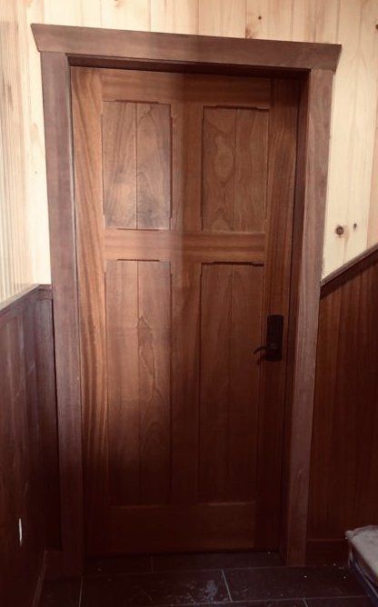 A wooden door with a black handle is in a room with wood paneling.