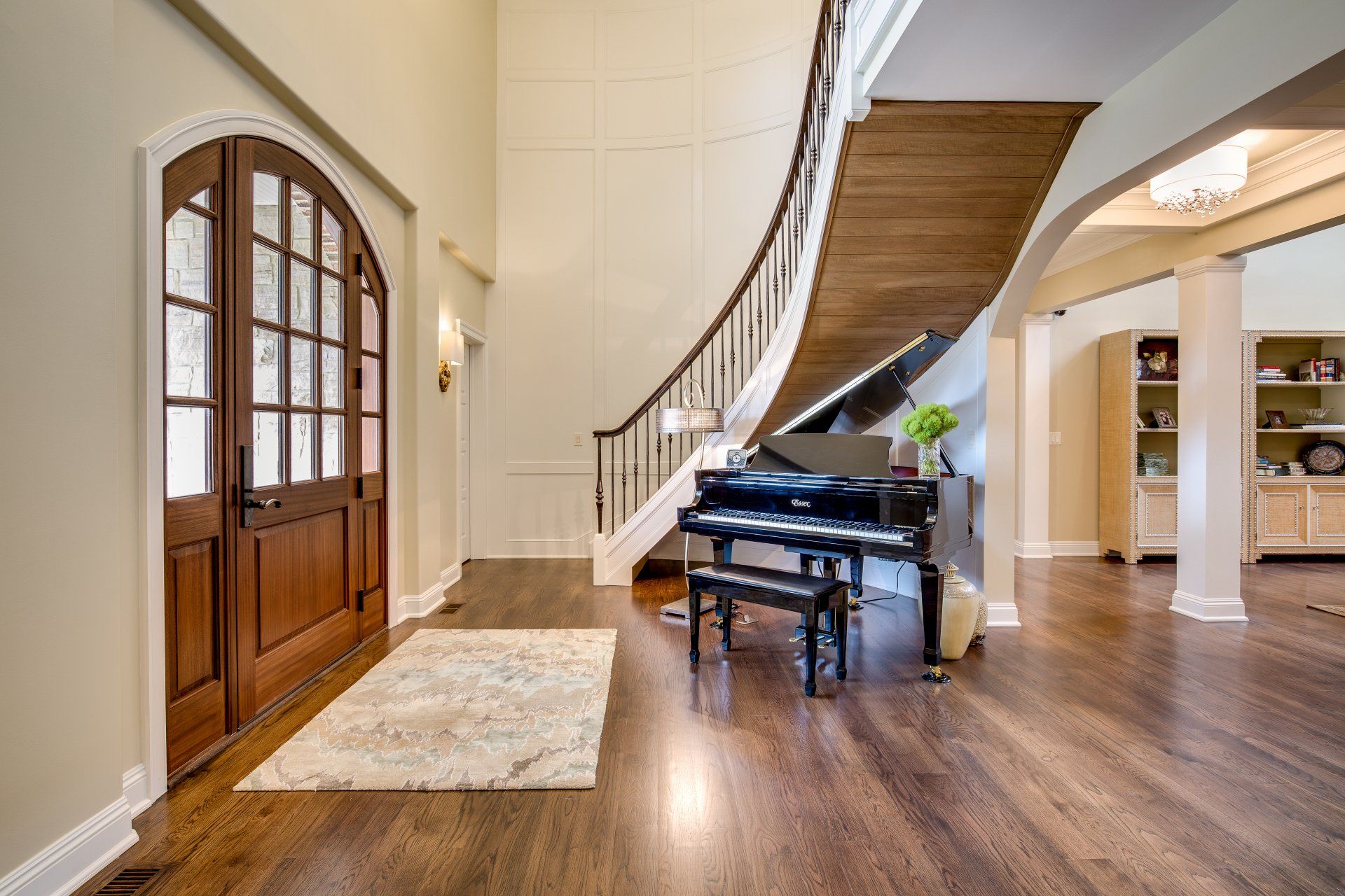 A grand piano is sitting in a hallway next to a curved staircase.