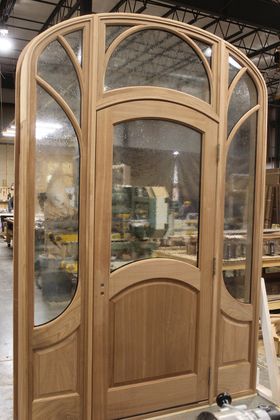 A wooden door with arched windows is being built in a factory.
