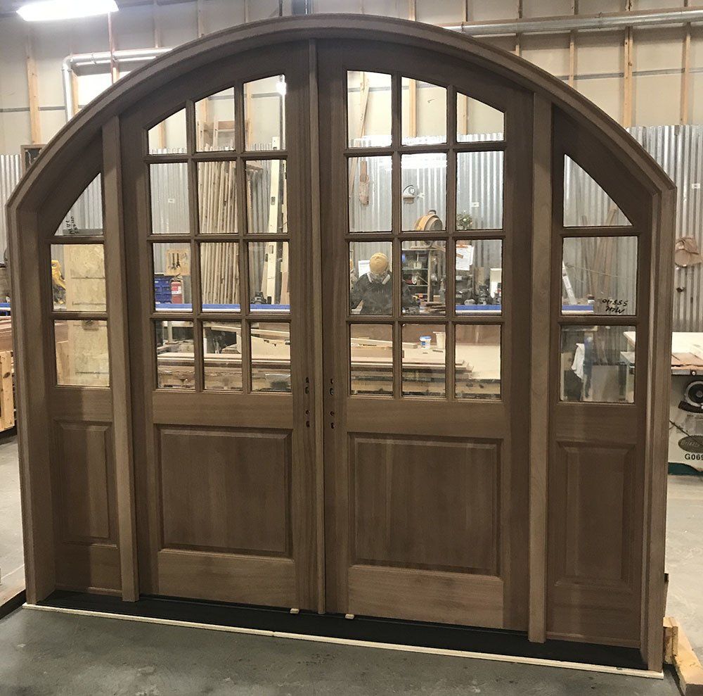 A large wooden door with arched windows is sitting in a workshop.