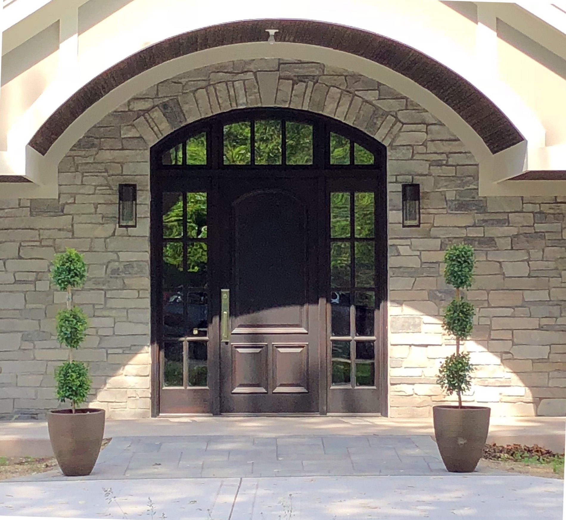 A stone building with a black door and two potted plants in front of it