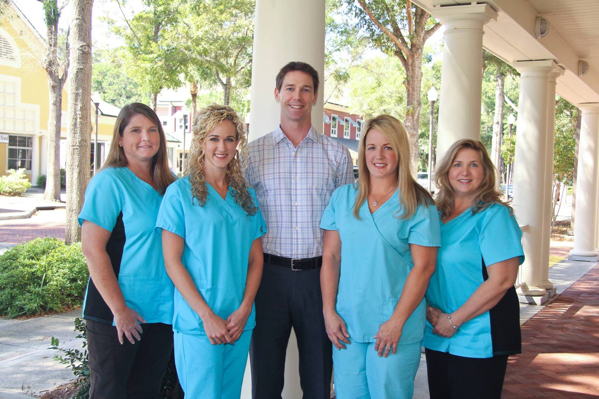 Five healthcare staff in turquoise scrubs standing outdoors under a covered walkway