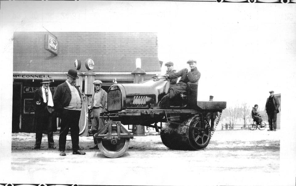 A black and white photo of men standing around an old tractor