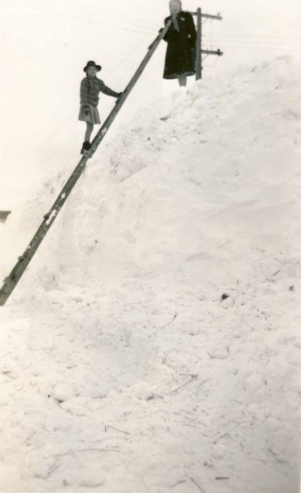 A black and white photo of a person standing on a ladder in the snow.