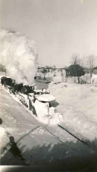 A black and white photo of a train going through the snow.