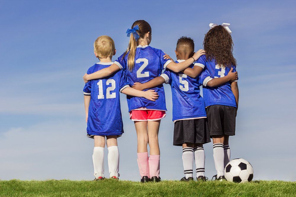 A group of young children are hugging each other on a soccer field.