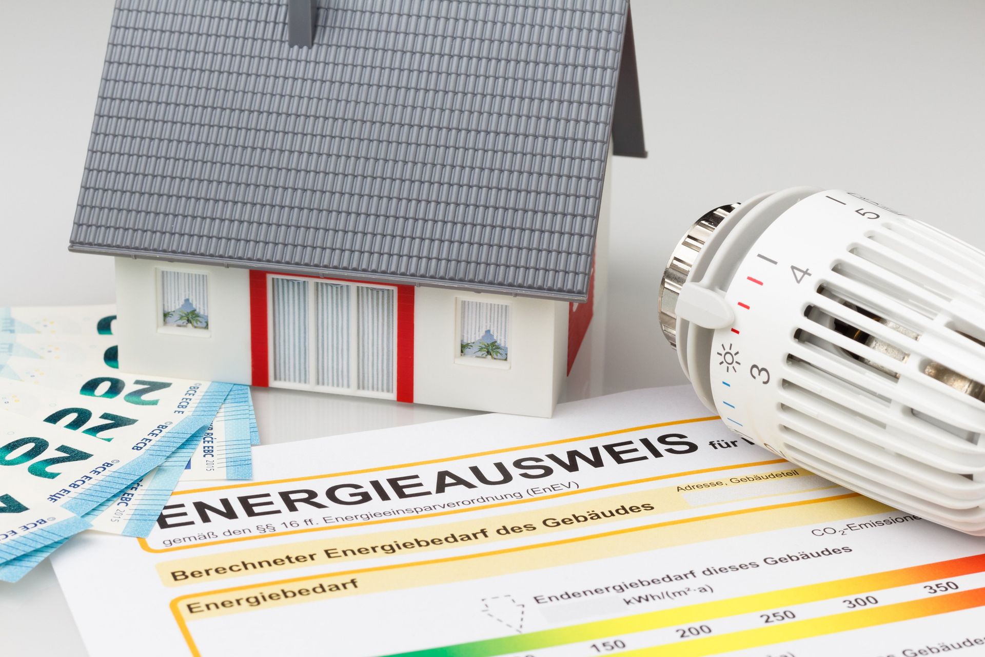 Musterhaus neben einem Energieausweis, Geld und einem Thermostat.