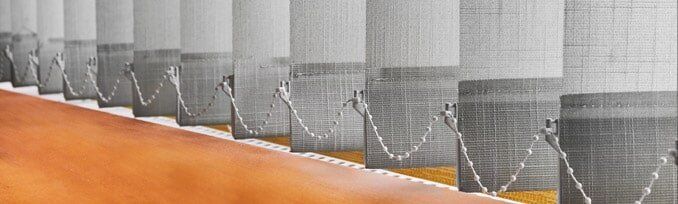 Row of vertical blinds with a wavy pattern in front of an orange surface.