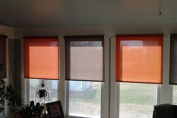 Orange and brown roller shades on windows inside a room, partially blocking sunlight.