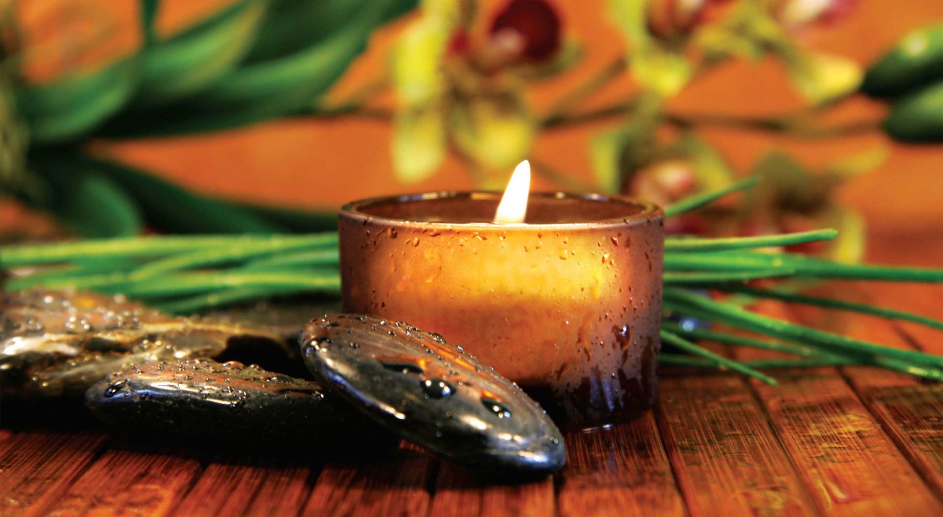 A candle is sitting on a wooden table next to some rocks and flowers.
