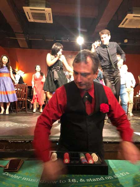 A man in a red shirt and black vest is standing in front of a table with a box of cigarettes on it.