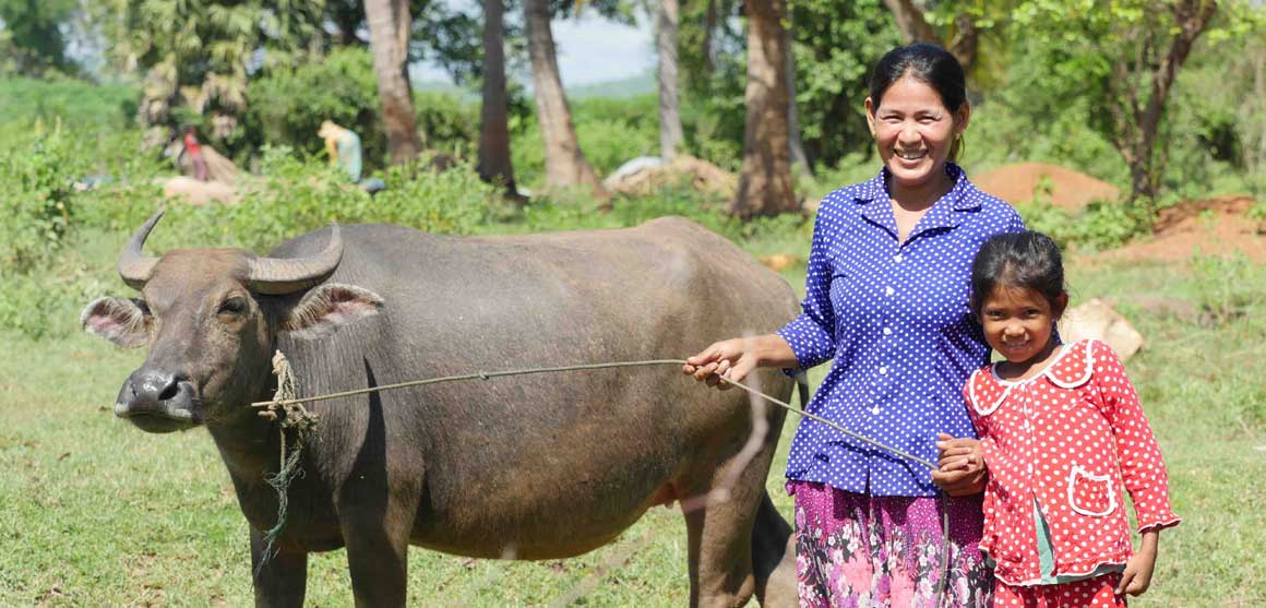 A woman and a child are standing next to a water buffalo in a field.
