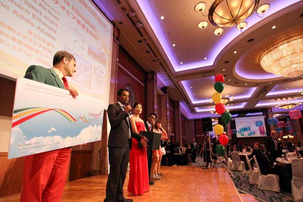 A group of people are standing on a stage in a large room with balloons.