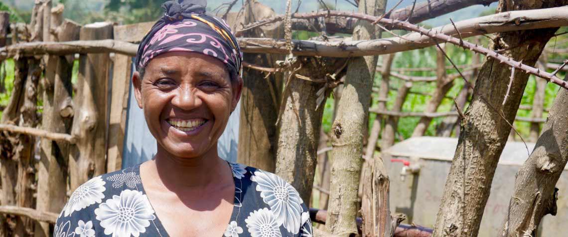 A woman is smiling in front of a wooden fence.