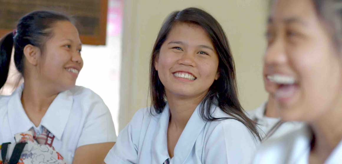 A group of young women are sitting in a classroom and smiling.