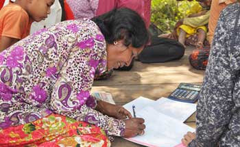A woman is sitting on the ground writing on a piece of paper.