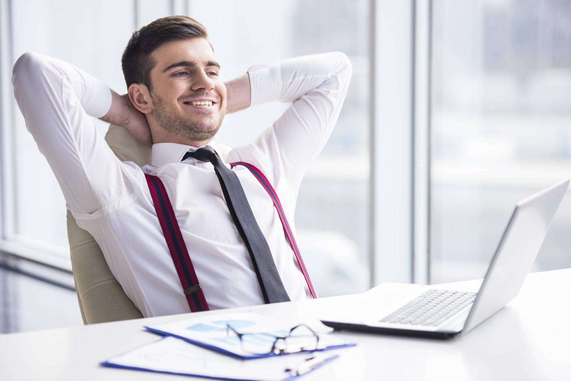 A man is sitting at a desk with his hands behind his head.