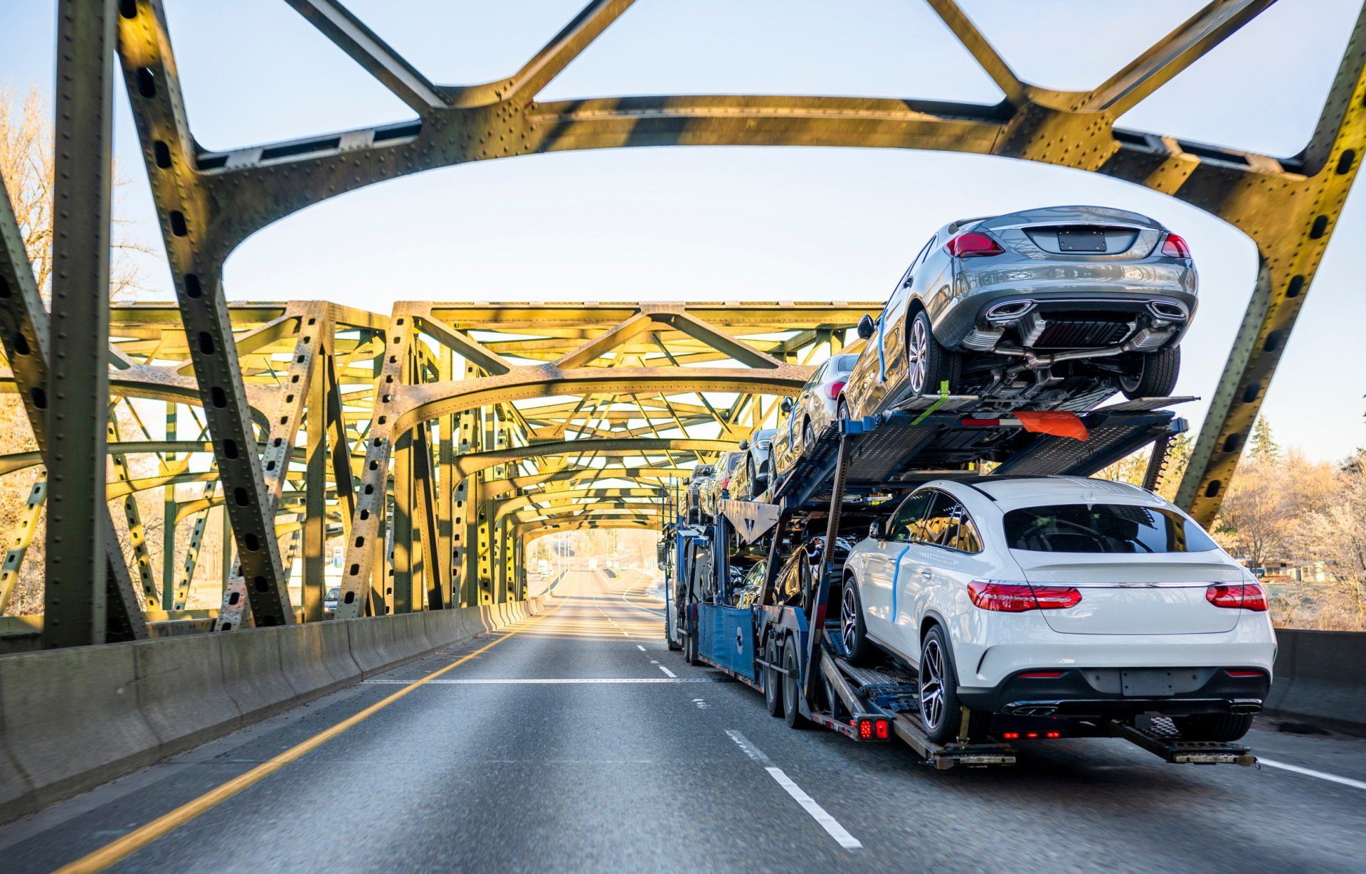 A truck is carrying two cars on top of each other on a highway.