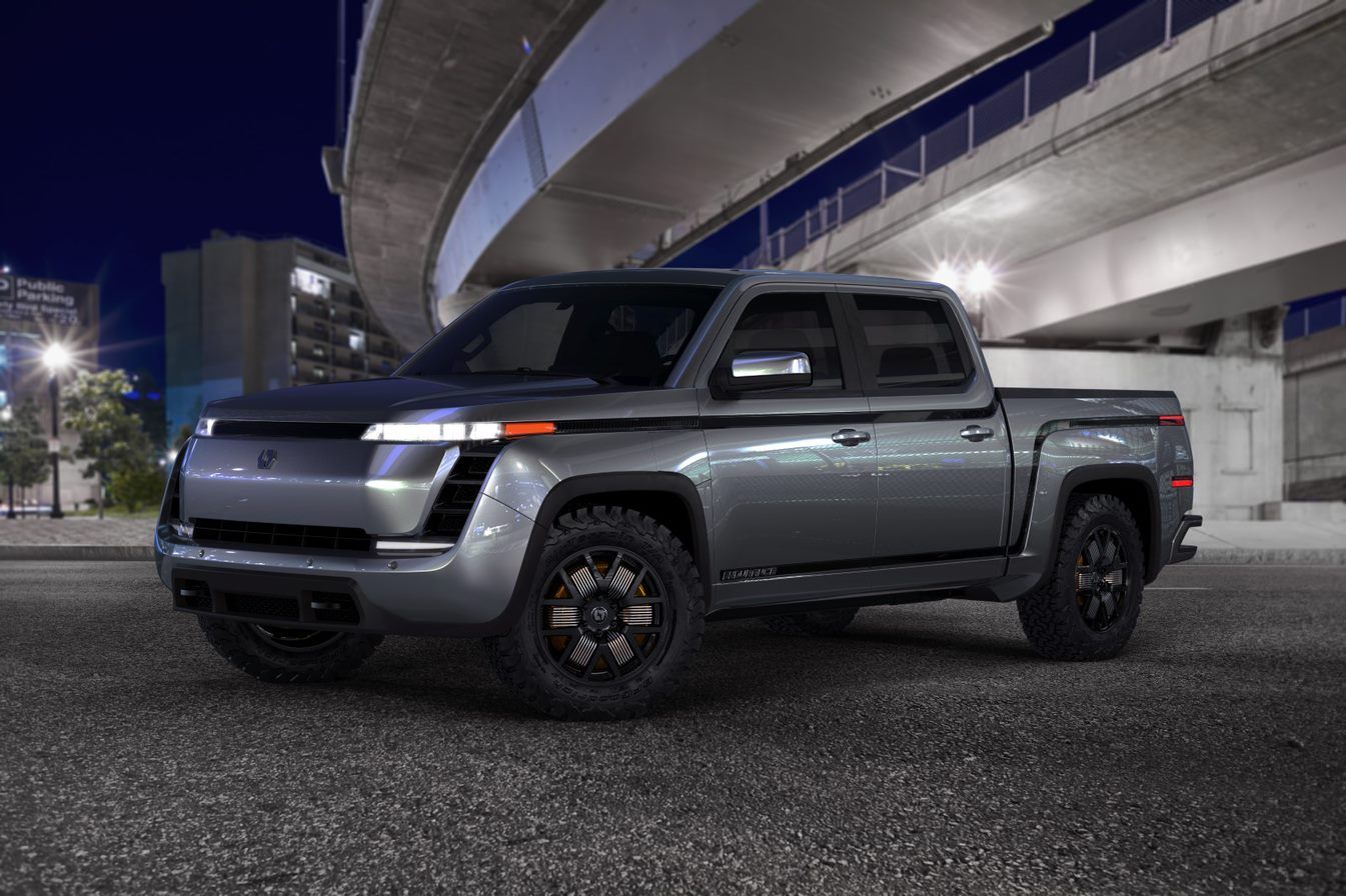 A gray truck is parked under a bridge in a city at night.