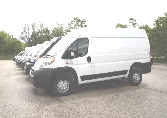 A row of white vans are parked in a parking lot.
