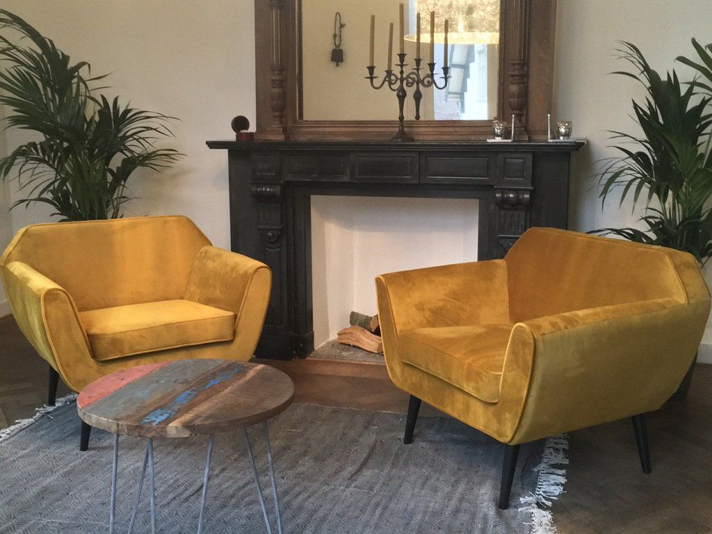 Twee gele stoelen zitten voor een open haard.