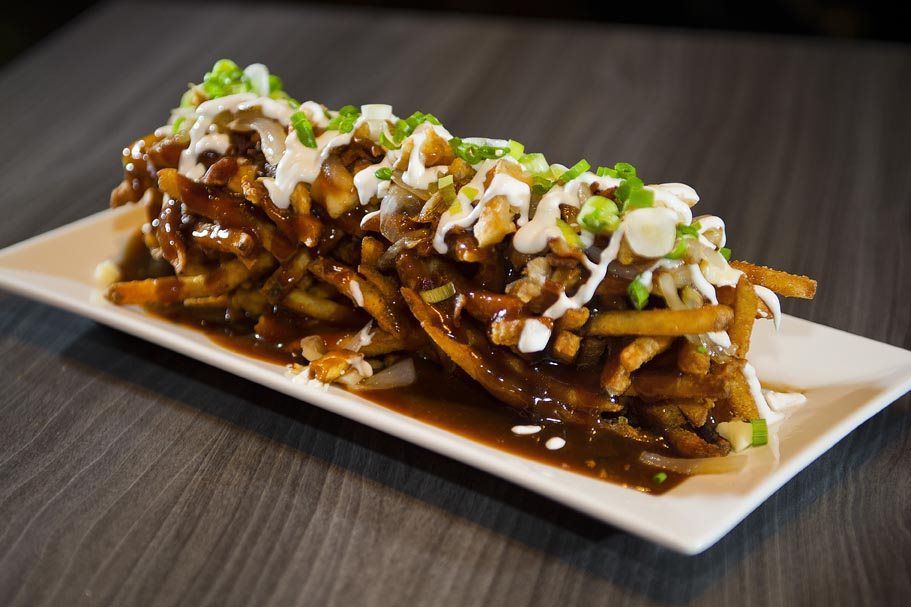 Loaded fries topped with sauce, sour cream, and green onions on a rectangular plate
