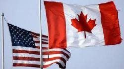 U.S. and Canadian flags waving against a cloudy sky