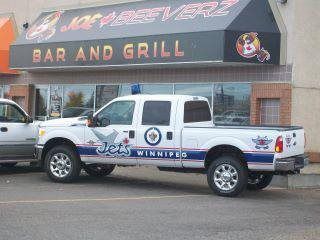 White pickup truck with Jets Wings livery parked outside a bar and grill storefront